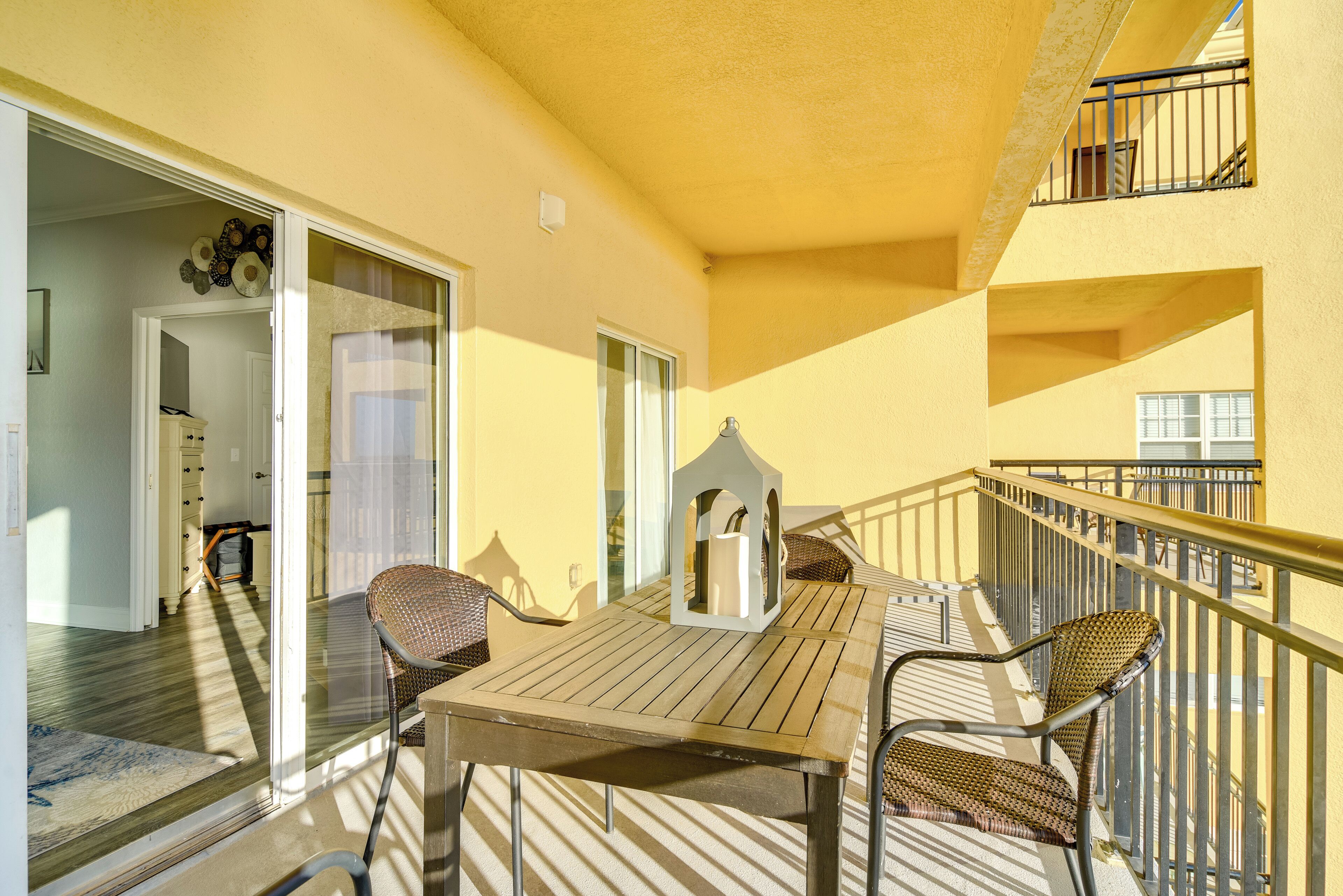 A balcony with a wooden table and chairs, a glass door leading to an interior room, and a railing.
