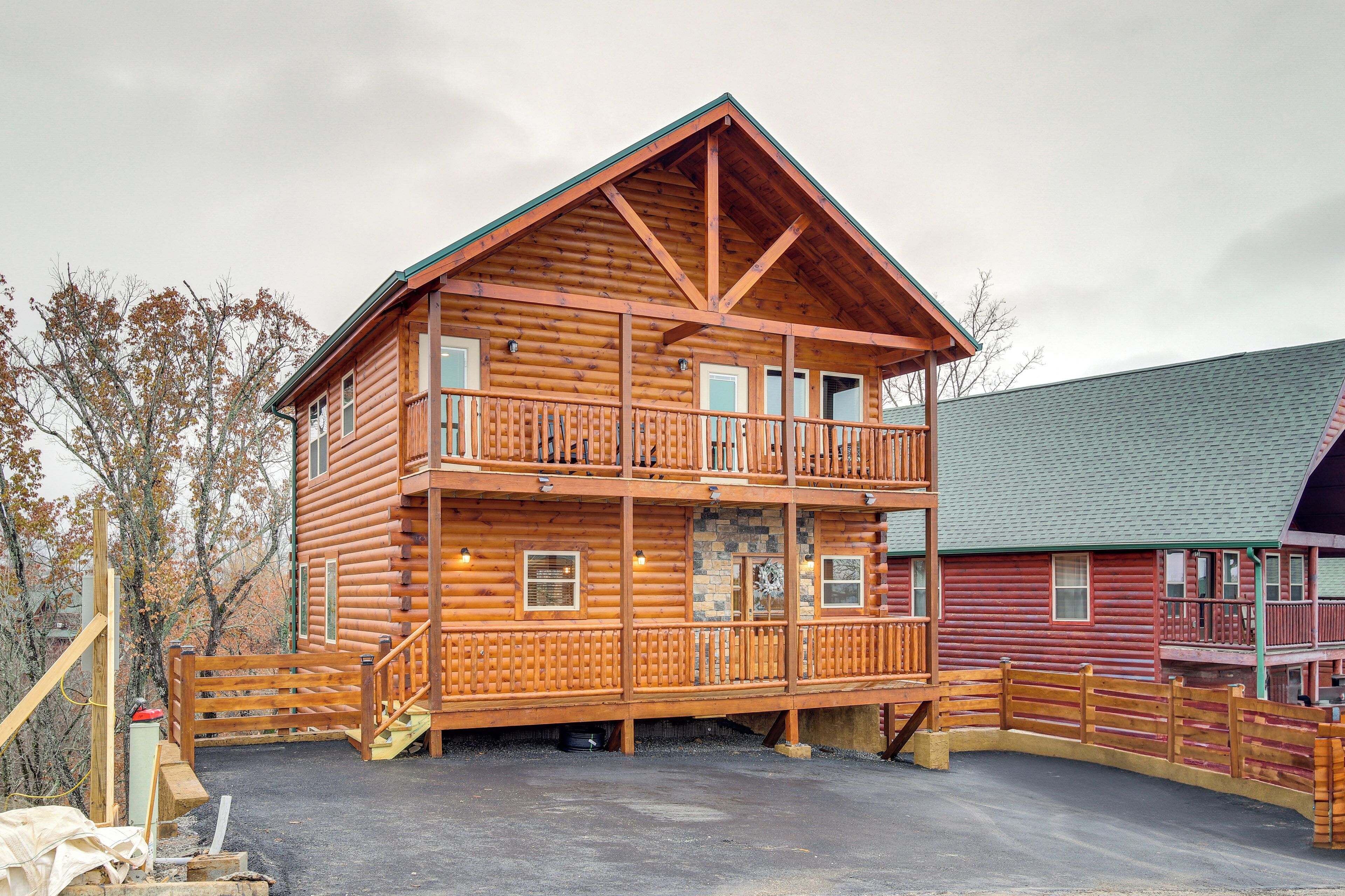 A two-story log cabin with a balcony on the upper floor, a stone foundation, and a covered porch area.