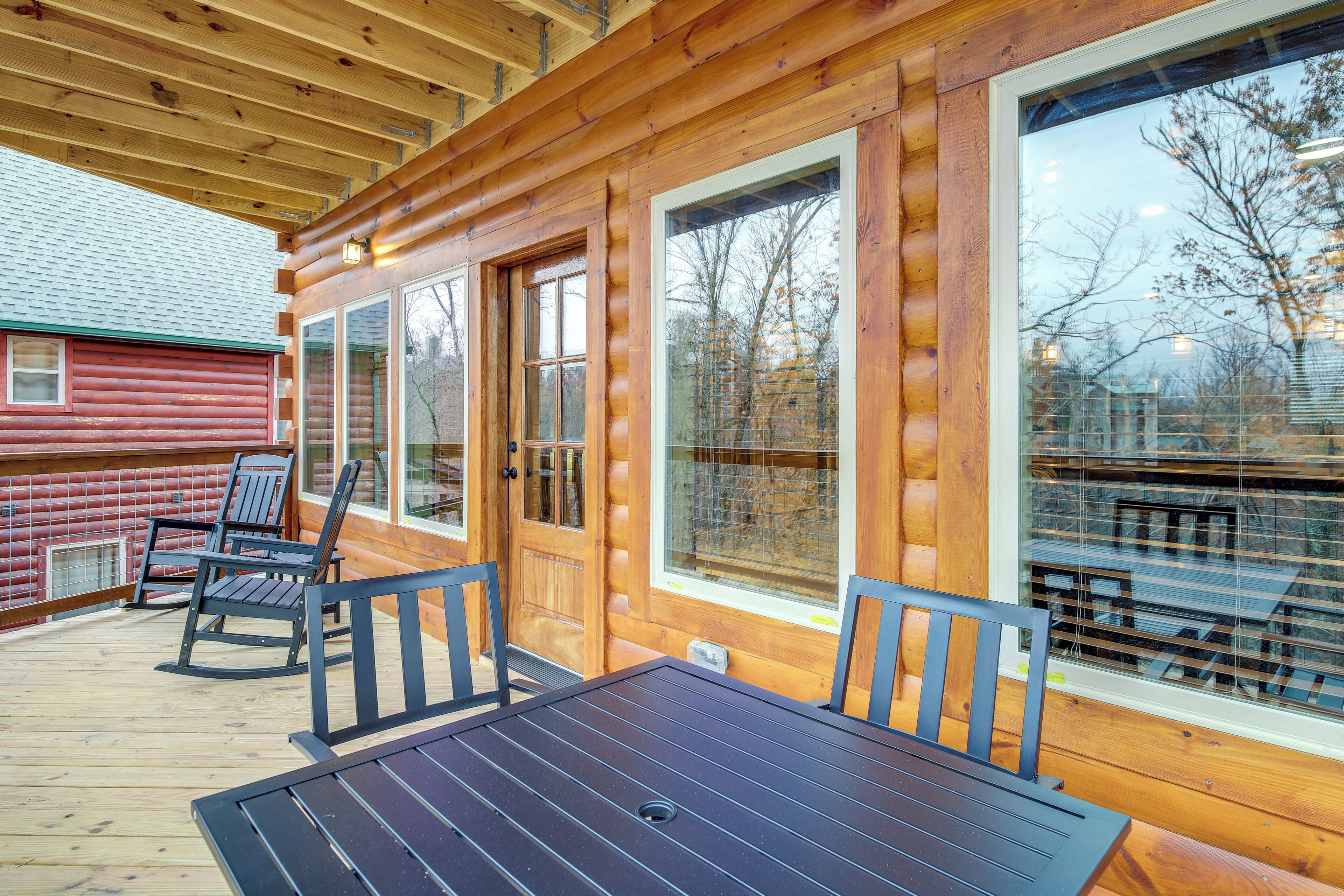 A wooden deck with a table and chairs, large windows, and a red building in the background.