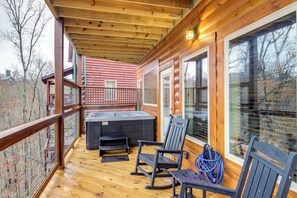 A wooden deck with a hot tub, two rocking chairs, and a covered area with large windows. - Hot Tub & Spectacular Views: Sevierville Cabin (Sevierville)