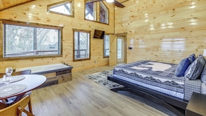 Interior de una cabaña de madera con una cama, una mesa de comedor y una bañera.