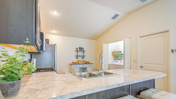 A kitchen with a marble countertop, stainless steel sink, and wooden cabinets. There are two stools and a potted plant on the counter. - Golf, Shop & Unwind: Lovely Home in The Villages! (Wildwood)