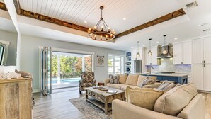 A spacious living room with a large sofa, a coffee table, and a wooden cabinet. There is a dining area with a blue table and chairs, and a kitchen with white cabinets and a stainless steel range hood. - Tranquility & Nearby Beach Access: Private Oasis (Santa Rosa Beach)