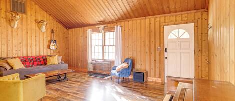 A wooden cabin interior with a piano, a sofa, a chair, and a dog cage.