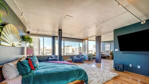Une chambre moderne dotée d’un grand lit, offrant une vue sur la ville et équipée d’un téléviseur à écran plat.