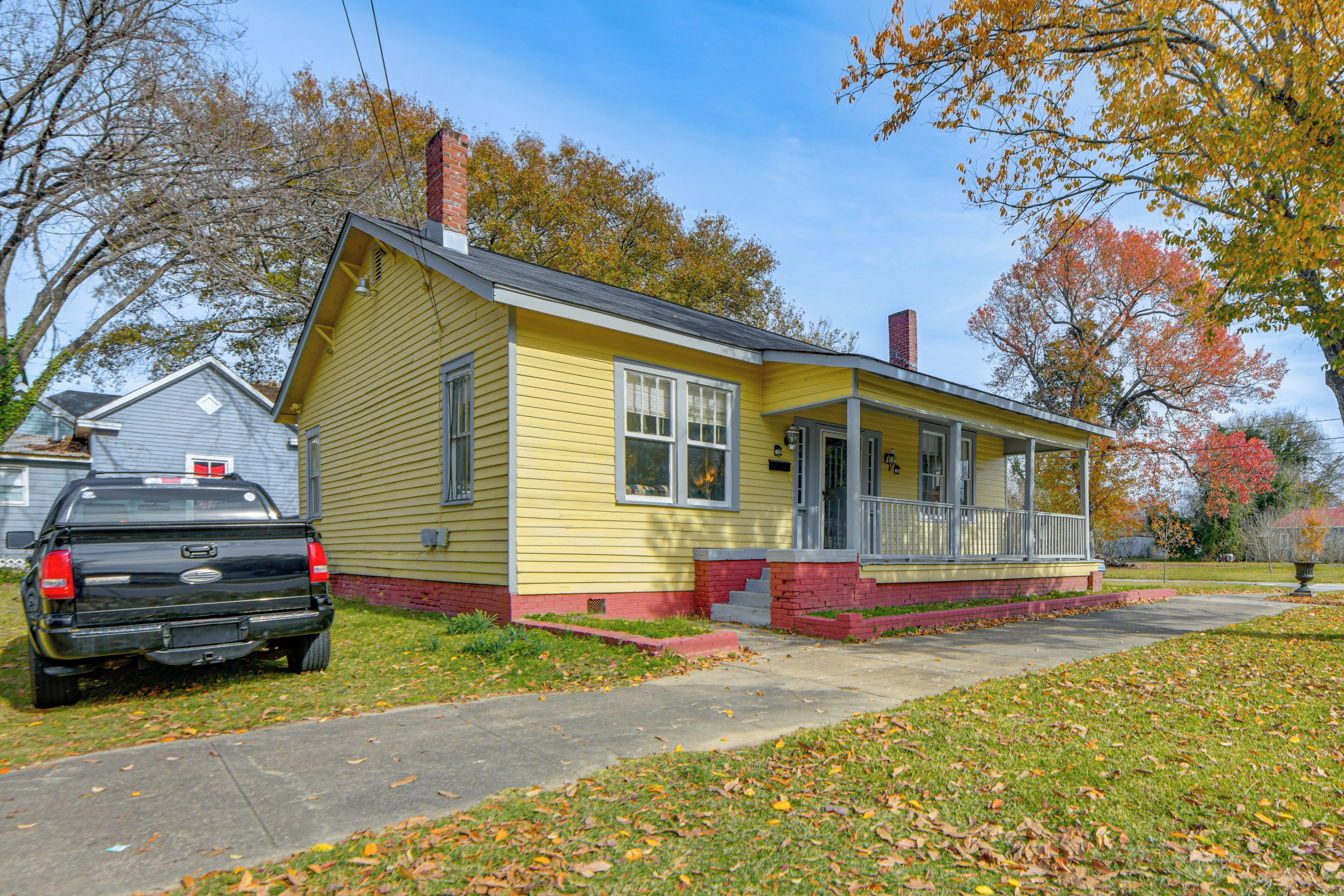 A yellow single-story house with a porch, a black pickup truck parked in front, and a clear sky.