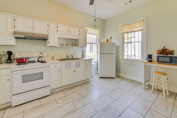 Una cocina con armarios blancos, estufa, refrigerador y microondas.