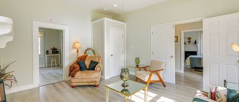 A spacious living area with a ceiling fan, a sofa, a coffee table, and a chair. There is a doorway leading to a kitchen and a bedroom.