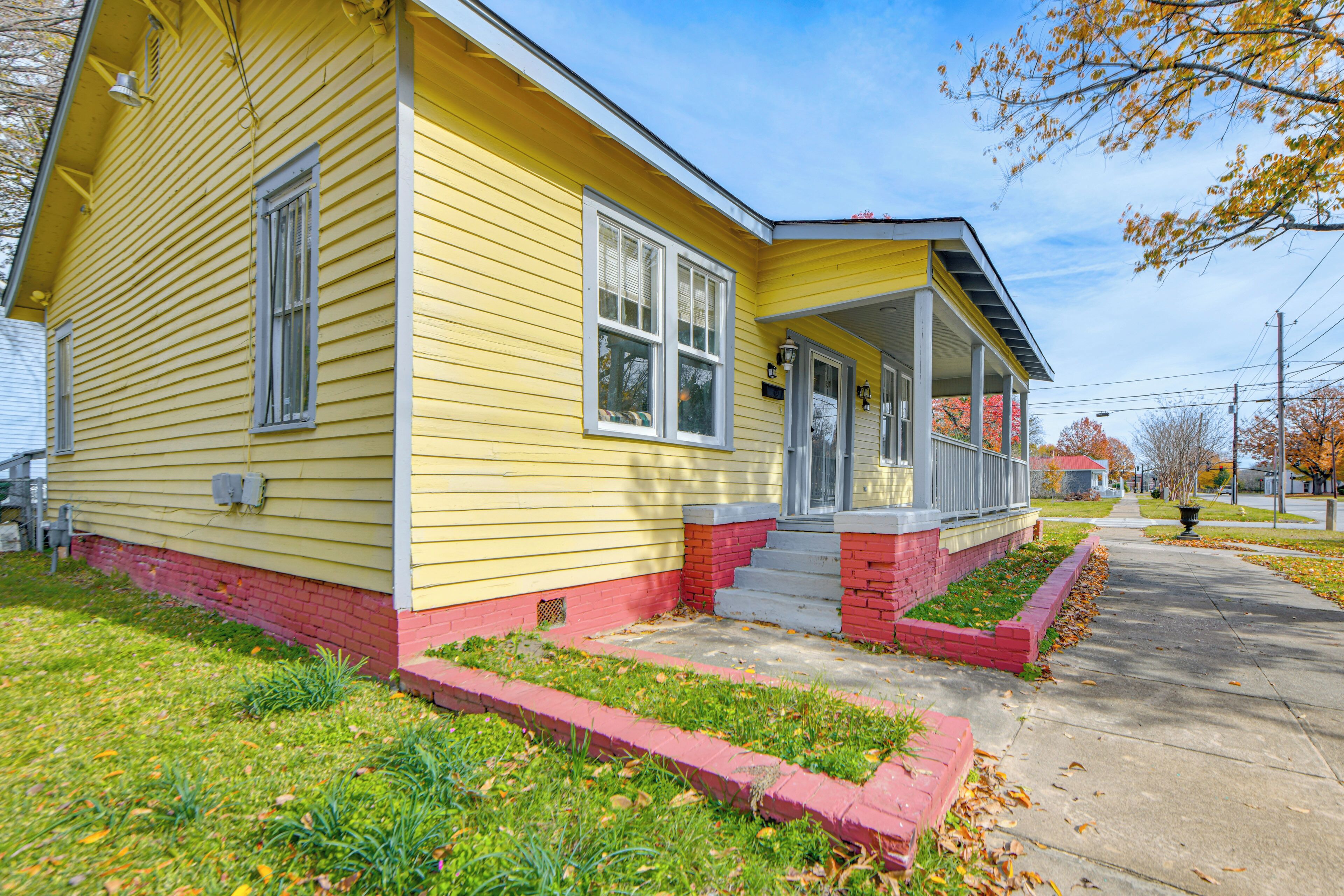 A yellow single-story house with a front porch, a small front yard, and a sidewalk leading to the street.