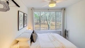 A bedroom with a bed, a ceiling fan, a window with a view of trees, and framed pictures on the wall. - Mtn Views + On-site Hiking Trails: Catskills Cabin (Round Top)