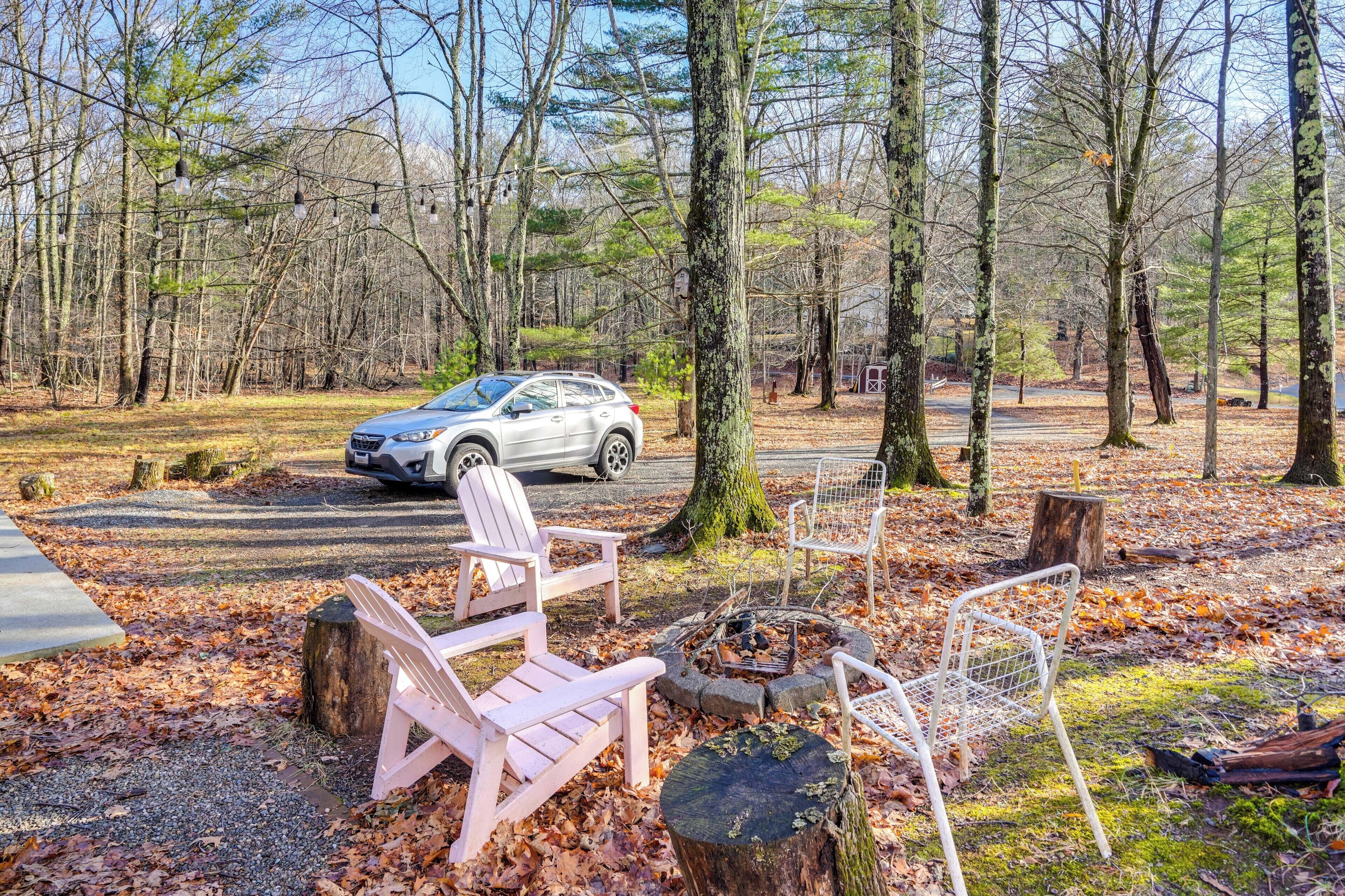 Ein Campingplatz mit einem Auto, zwei Adirondack-Stühlen, einer Feuerstelle und einem Picknicktisch.