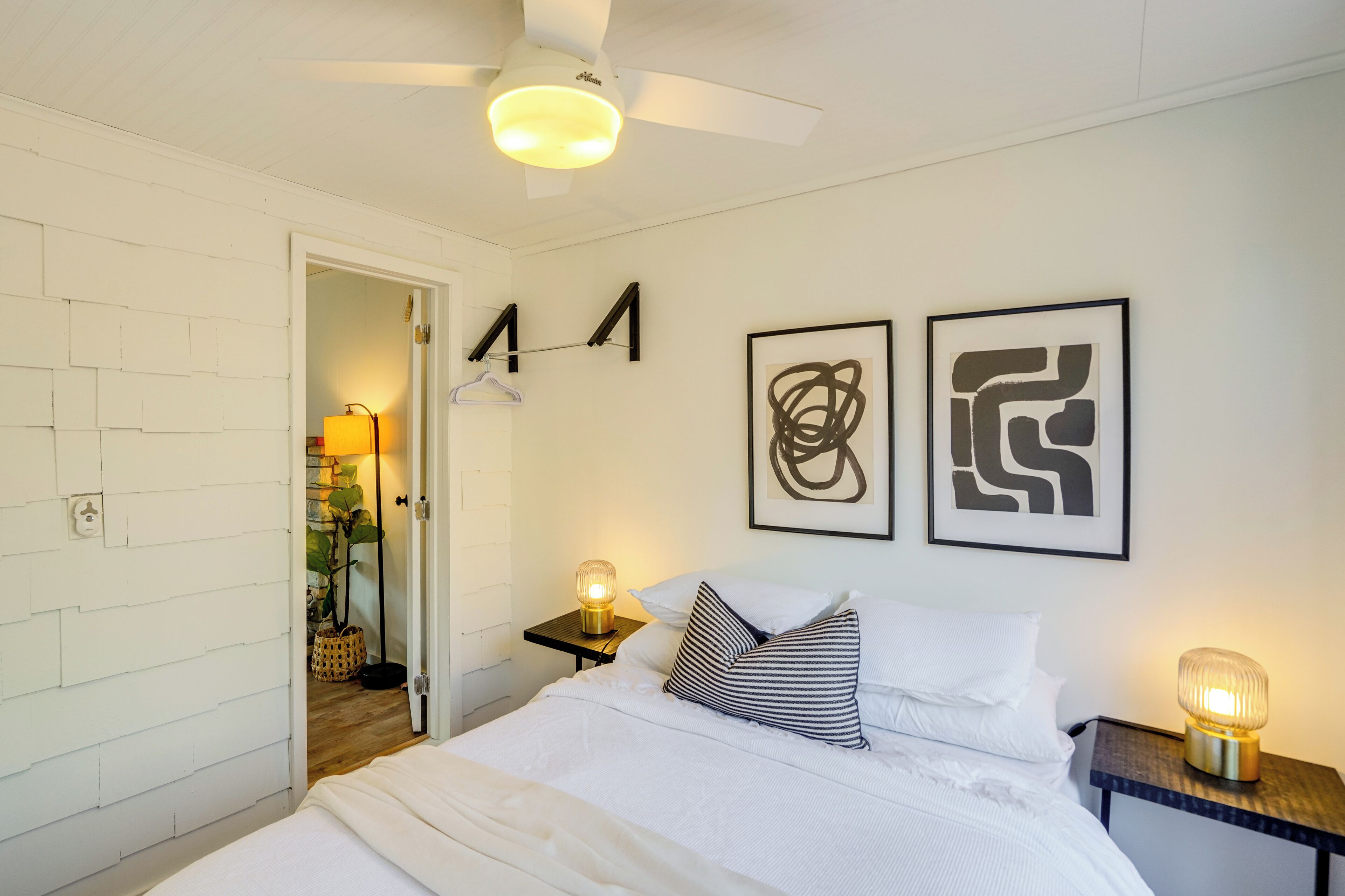 A bedroom with a bed, a ceiling fan, two wall-mounted light fixtures, and abstract wall art.