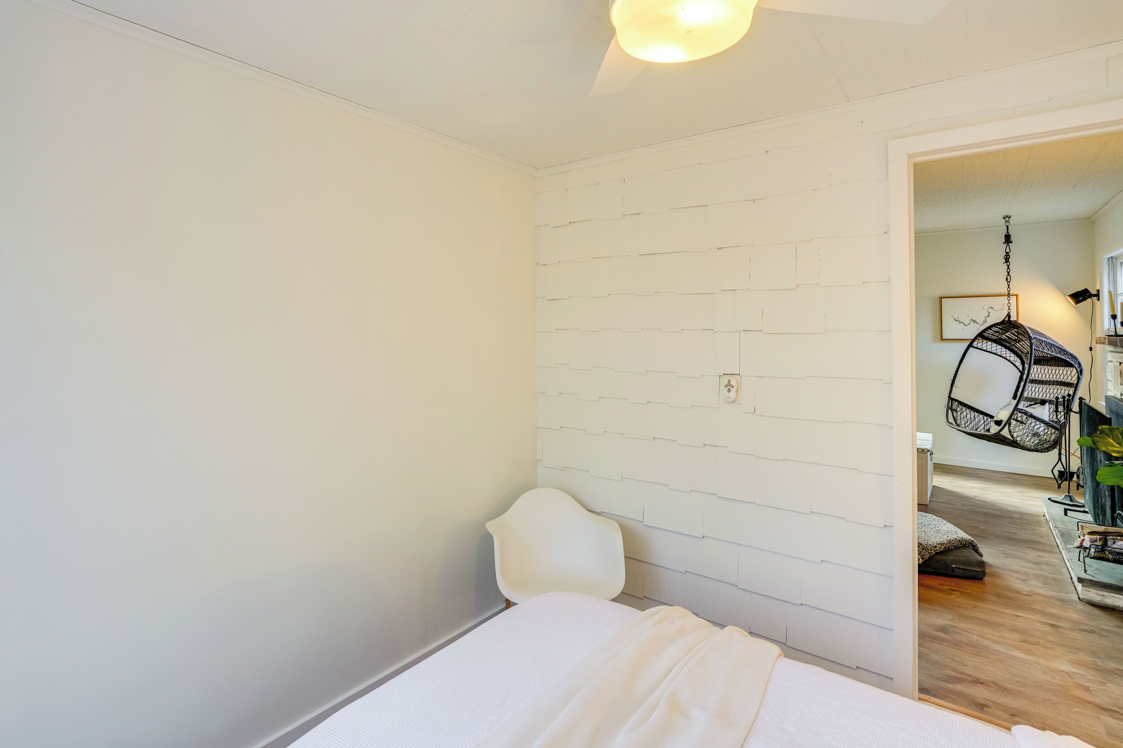 A bedroom with a white bed, a white chair, and a hanging chair in the corner.