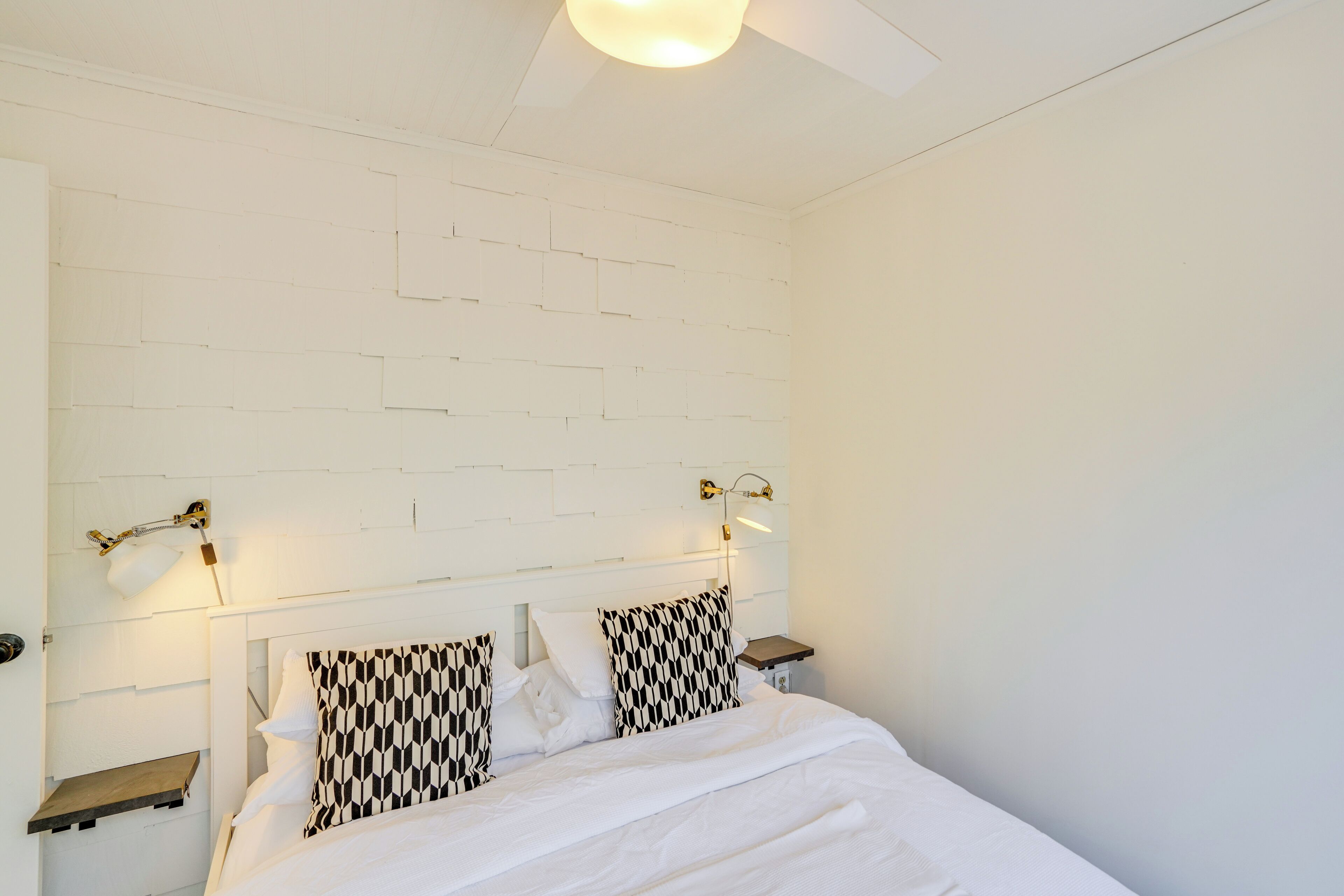A neatly made bed with white bedding, two patterned pillows, and a headboard with a white brick design. There are two bedside tables with lamps on either side of the bed.