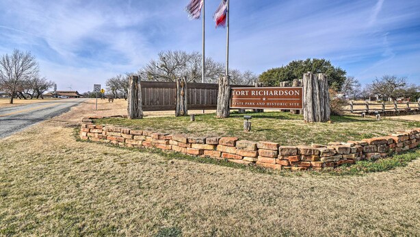 A sign for Fort Richardson State Park and Historic Site with two flags, a brick wall, and a clear sky. - 4 Miles to Lake Jacksboro: Cozy Texas Cottage (Jacksboro)