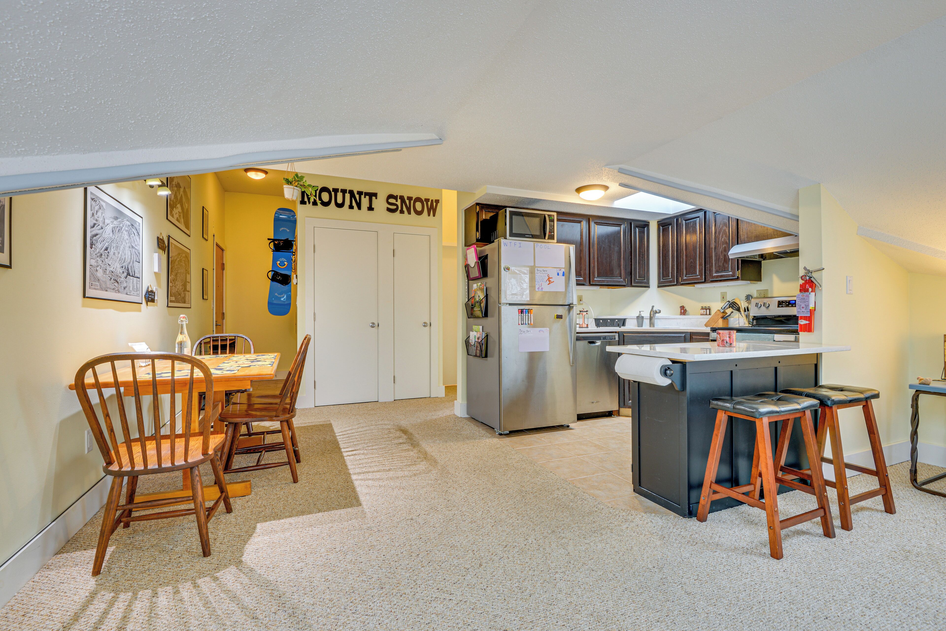 A compact kitchen with a dining area, featuring a refrigerator, microwave, and wooden chairs.