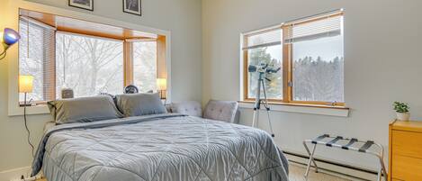 A bedroom with a bed, two windows, a desk, a lamp, and a radiator.