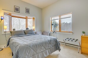 Une chambre à coucher avec un lit, deux fenêtres, un bureau, une lampe et un radiateur.