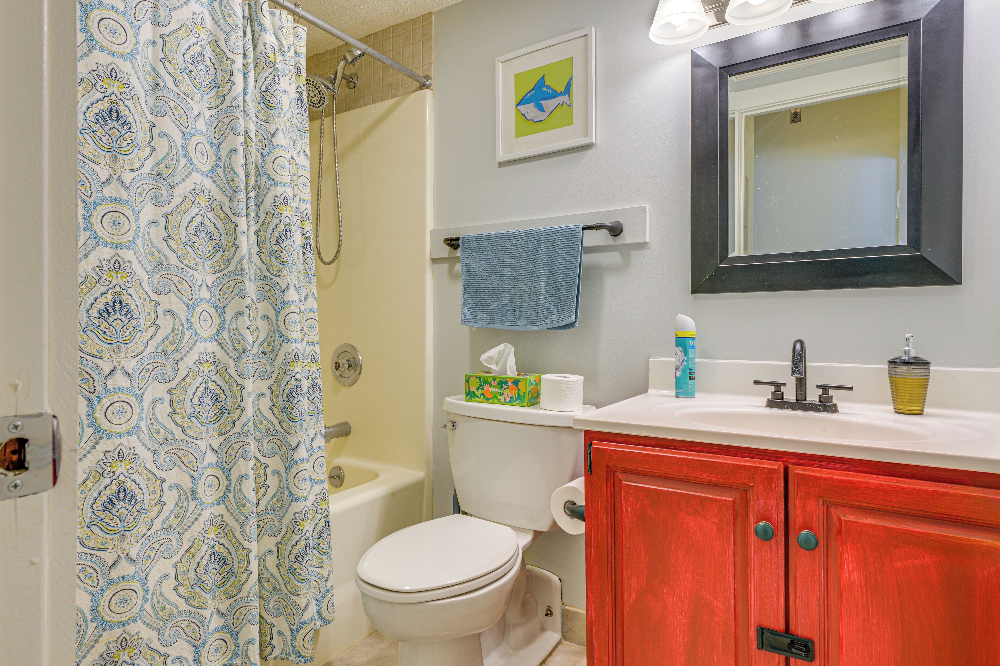 A bathroom with a shower curtain, toilet, sink, and red cabinets.