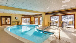 Una piscina interior con un reloj, sillas y ventanas que dan a una vista nevada.