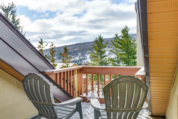 A balcony with two Adirondack chairs, a wooden railing, and a view of a snowy mountain range.
