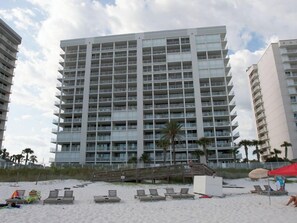 A high-rise hotel with multiple balconies and a beach area with sun loungers.