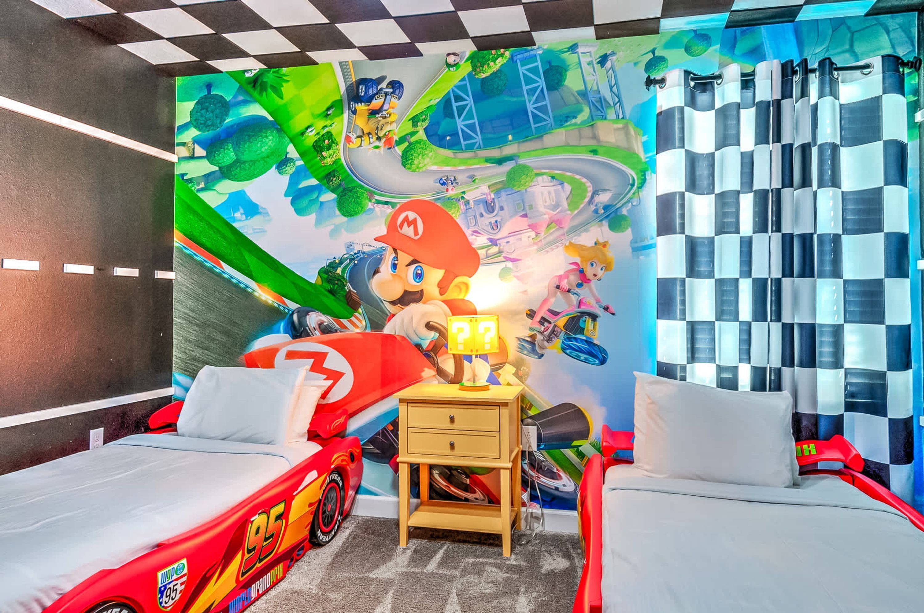 A bedroom with two beds, a mural of Mario Kart, and a checkered curtain.