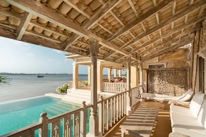 Un espacio al aire libre techado con piscina, sillones de descanso y vista al mar.