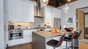 Une cuisine moderne avec des meubles blancs, des appareils en acier inoxydable et un îlot central doté de tabourets de bar.