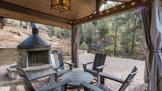 An outdoor patio with a stone fireplace, Adirondack chairs, and a string of lights. - Hot Tub | Sauna | Game Room!  5 Acres - 2 miles from Downtown (Durango)