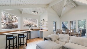 A spacious living area with a large L-shaped sofa, a kitchen with a bar area, and multiple windows offering views of the outdoors. - Hot Tub | Sauna | Game Room!  5 Acres - 2 miles from Downtown (Durango)