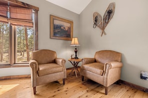 A room with two leather armchairs, a painting, a lamp, and a window with a view of trees.