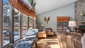A cozy living room with a large window, a stone fireplace, and a blue sofa.