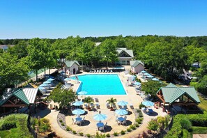 A large swimming pool surrounded by lounge chairs and umbrellas, with a building in the background.