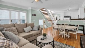 Ein geräumiges Wohnzimmer mit einem beigefarbenen Sofa, einem Couchtisch und einer Treppe, die in einen Essbereich mit einem weißen Tisch und Stühlen führt.
