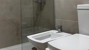 A modern bathroom with a glass-enclosed shower, a white toilet, and a bidet. - estudio Centro (San Carlos de Bariloche)