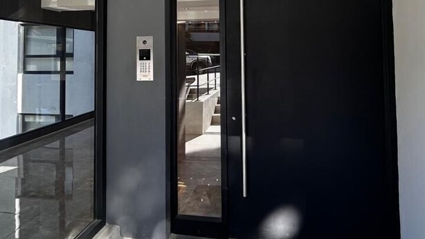 A modern entrance with a glass door, a keypad lock, and a view of a parking area. - estudio Centro (San Carlos de Bariloche)