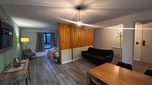 A modern living room with a wooden dining table, a black sofa, and a TV mounted on the wall. - estudio Centro (San Carlos de Bariloche)