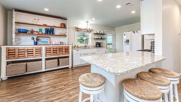 A modern kitchen with white cabinetry, a marble island, wicker stools, and built-in shelves. - Tranquil home w/ firepit near beach (Port St. Joe)