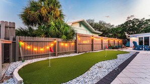 A backyard with a wooden fence, artificial grass, and a patio area with chairs and a table. - Tranquil home w/ firepit near beach (Port St. Joe)