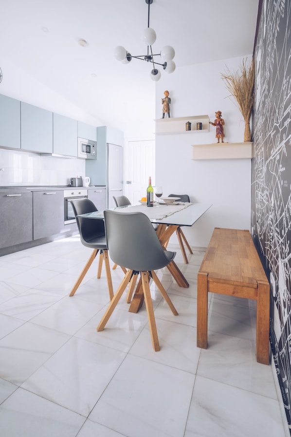 A modern kitchen with white cabinets, a dining area with a wooden table and chairs, and a decorative wall with a map. - "Exclusive Penthouse Living Elegance Meets Modern Design" (Gibraltar)