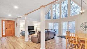 A spacious living room with a wooden floor, a sofa, a television, and a dining area with chairs and a table. - Deerfield Hideaway At Old Rocky 5 Bedroom Home (La Follette)
