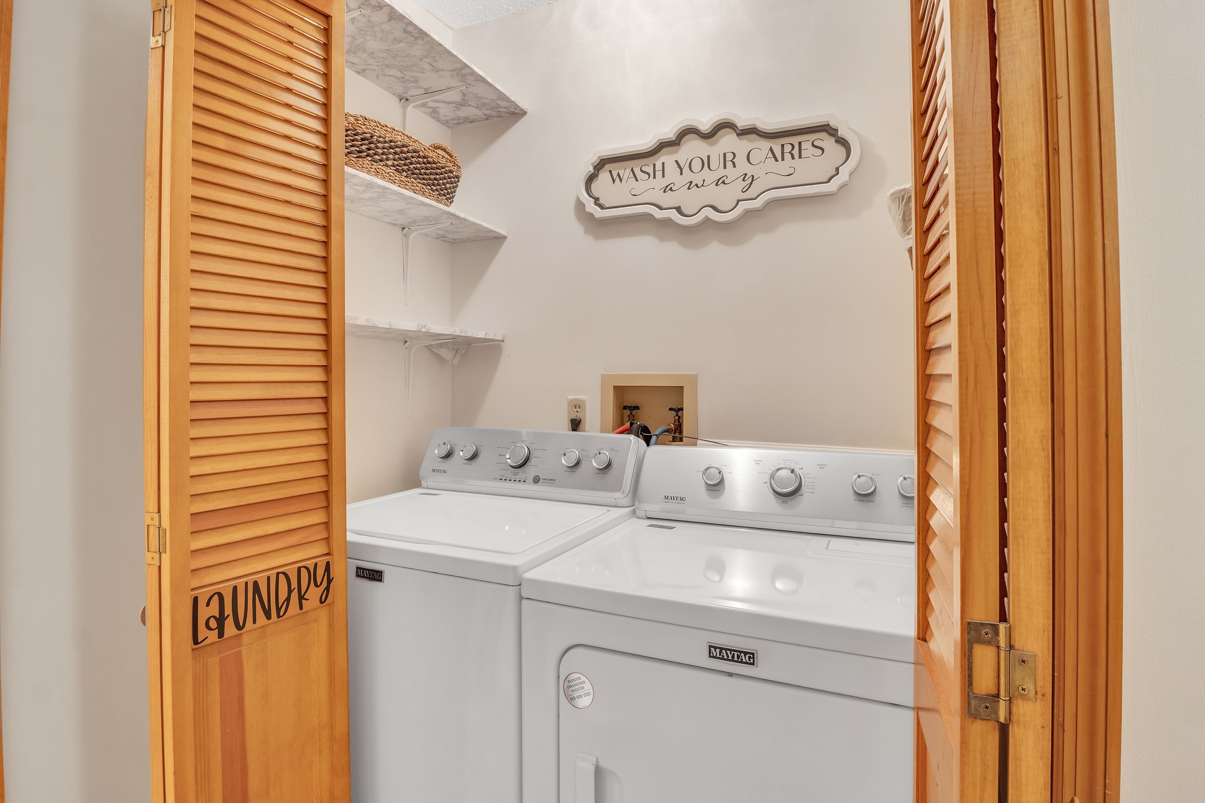 A laundry area with two white front-loading washing machines, a wooden door labeled "Laundry," and a wall sign that says "Wash Your Car Away."
