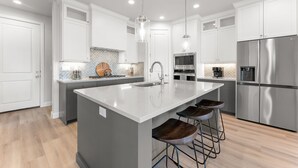 Una cocina moderna con armarios blancos, electrodomésticos de acero inoxidable, una isla grande con taburetes e iluminación colgante.