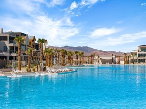 A resort pool with palm trees and modern buildings, surrounded by mountains. - Oasis Retreat 5 Bedroom Townhouse (St. George)
