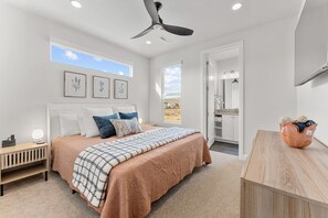 Een slaapkamer met een bed, nachtkastje, kunstwerk aan de muur, plafondventilator en uitzicht op het omliggende landschap.
