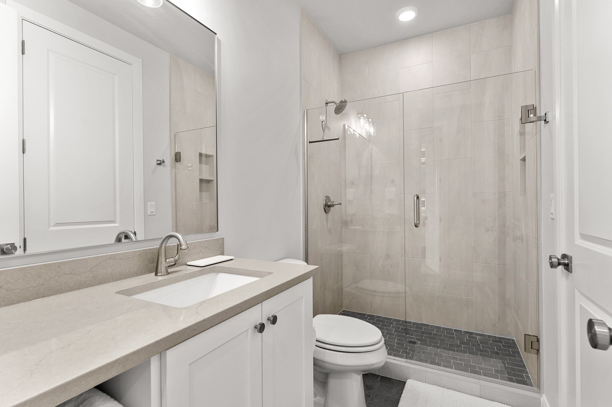 A modern bathroom with a large mirror, two sinks, a toilet, and a glass-enclosed shower.