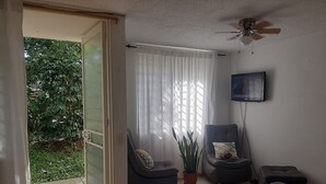 En stue med en skydedør til en balkon, en loftsvift og et fjernsyn på væggen.