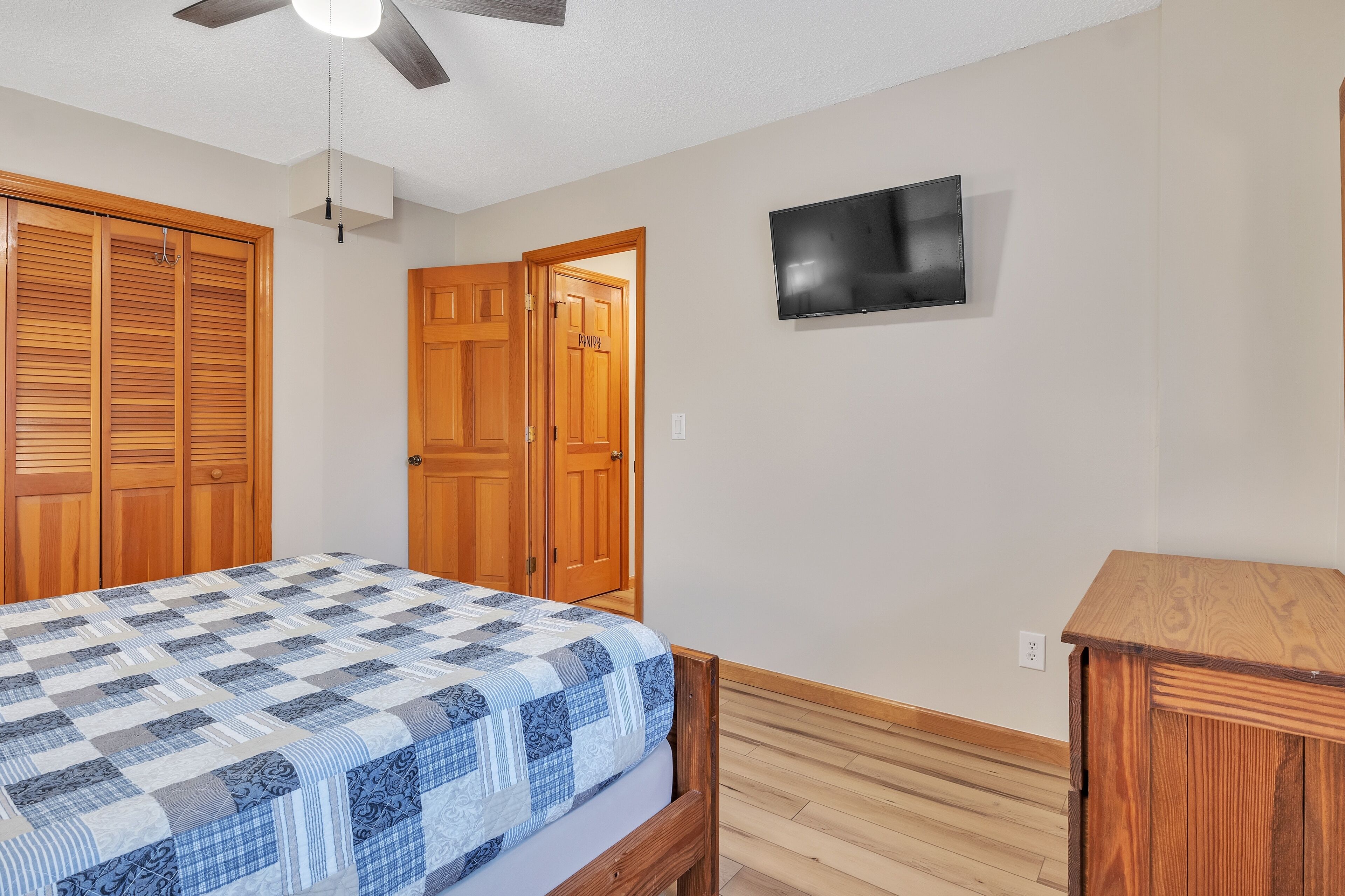 A bedroom with a bed, wooden wardrobe, and a television on the wall.