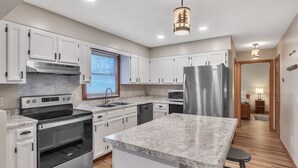 A modern kitchen with white cabinets, stainless steel appliances, and a marble countertop. - Deerfield Hideaway At Old Smokey 5 Bedroom Home (La Follette)
